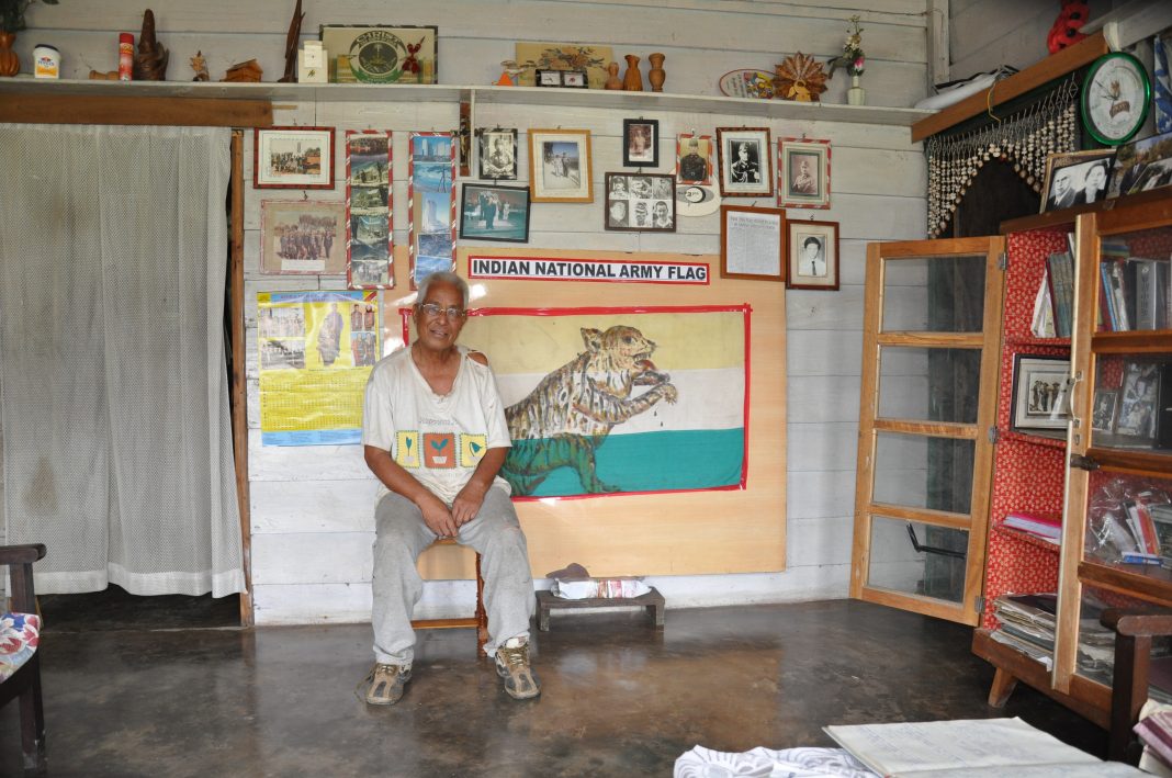 Shishak sitting at his home in Manipur with the first flag of Indian Independence as hoisted by Netaji Subhas Chandra Bose's Indian National Army in the background. Photo courtesy: Anil Dhir